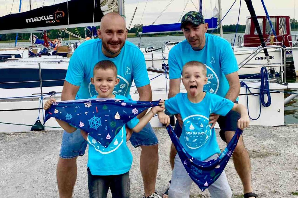 Ojcowie z dziećmi w koszulkach firmowych na rejsie mazurskim.