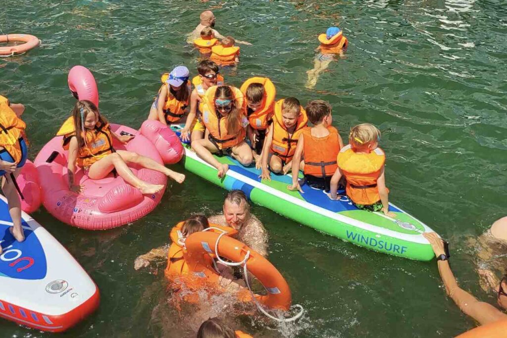 Dzieci w kamizelkach bawiące się na jeziorze Niegocin podczas rejsu rodzinnego.
