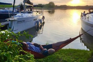 Żeglarz odpoczywający w hamaku między jachtami o zachodzie słońca na Mazurach