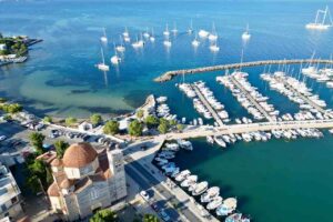 Port i kotwicowisko na wyspie Aegina — widok z drona na marinę, kościół i jachty stojące na turkusowej wodzie.