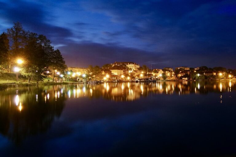 Ryn nocą – panorama miasta i jeziora Ryńskiego z odbiciem świateł w wodzie.