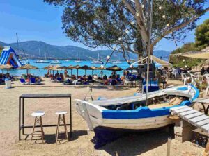 Plaża Russian Bay na Poros z leżakami, barem i widokiem na turkusową zatokę pełną zakotwiczonych jachtów.