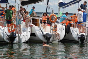 Jachty na Mazurach ustawione w tzw tratwę. Uczestnicy rejsu szykuję się na wejście do wody w kapokach.